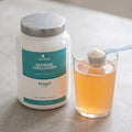 Marine Collagen tub beside a glass of orange drink and a scoop